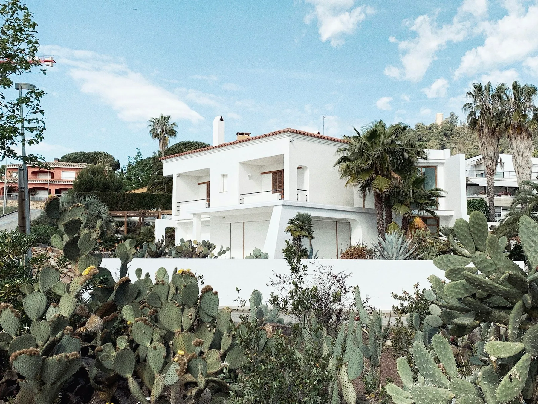 A white hillside villa with terraces, surrounded by prickly pear and palms