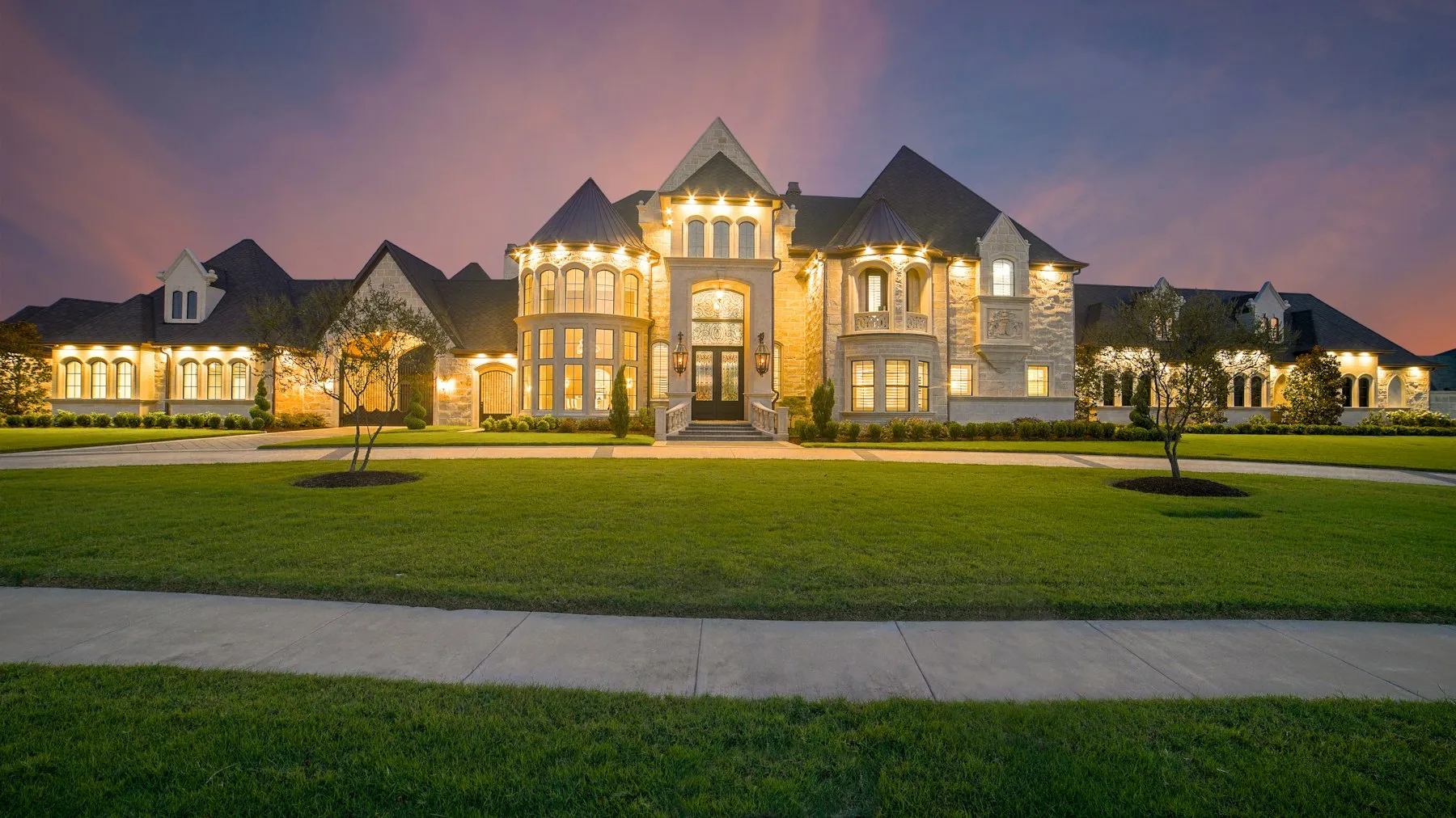 A large Georgian country house lit at dusk across a wide lawn