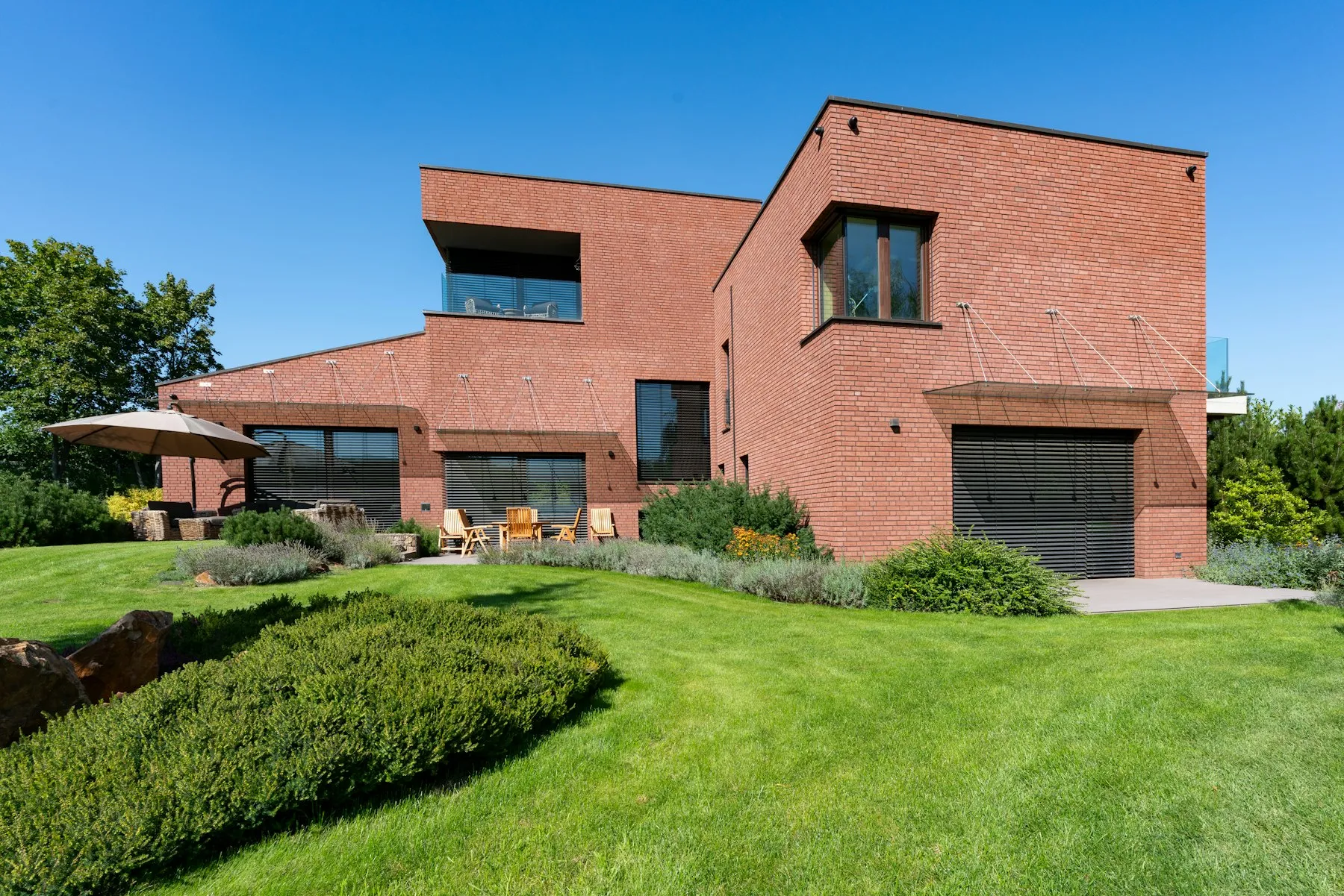 A low red brick modernist house with a clipped lawn in front of it